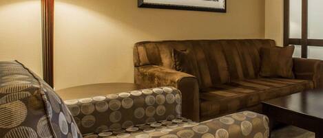 A room with a sofa, a patterned armchair, a lamp, and a framed picture on the wall.