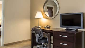 Ein Hotelzimmer mit Schreibtisch, Stuhl, Lampe, Spiegel und Fernseher.