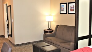A hotel room with a sofa, a small table with a lamp, a chair, and a bed. - Comfort Suites Huntersville near Lake Norman (Huntersville)