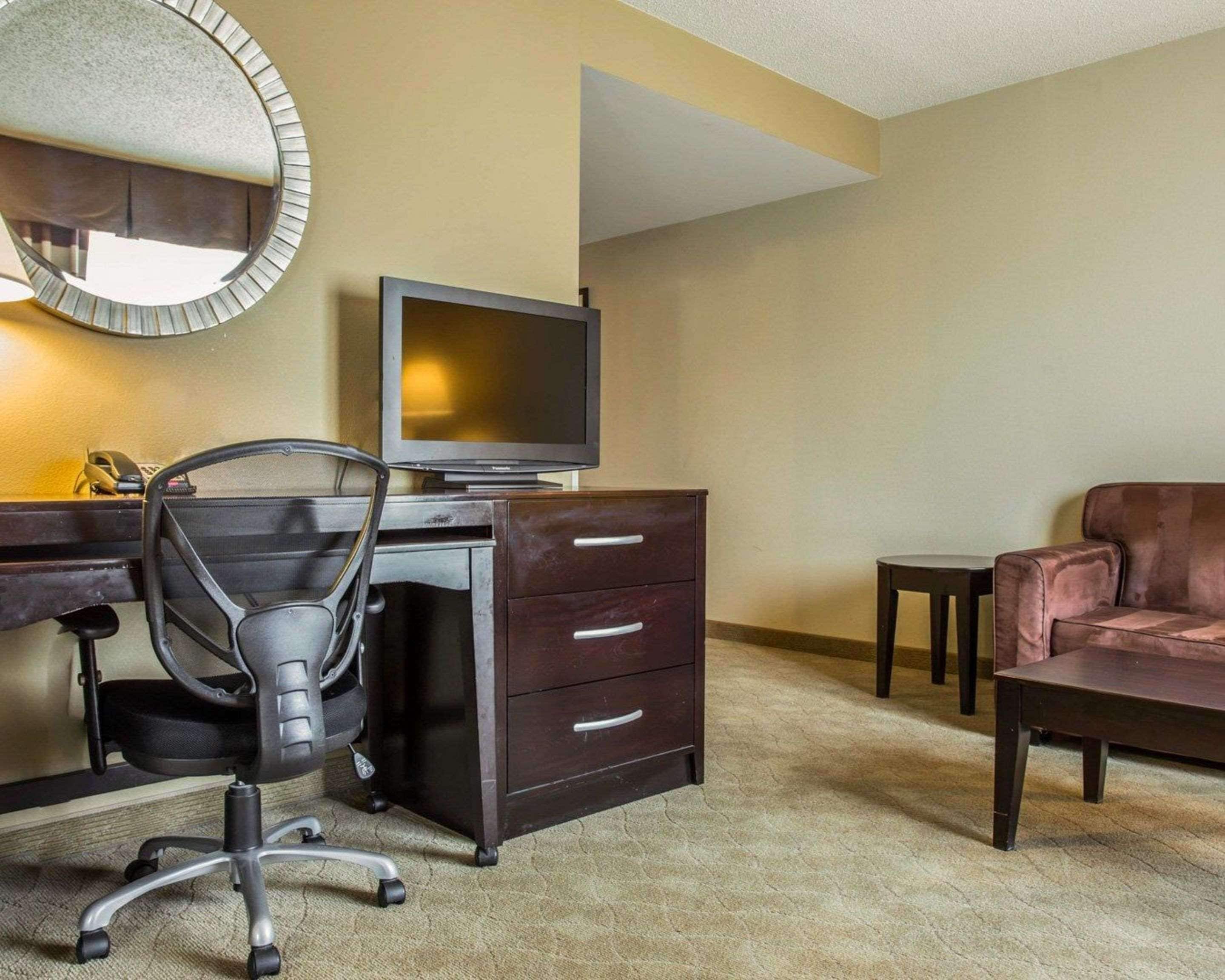Quarto de hotel com escrivaninha, cadeira, televisão e sofá.
