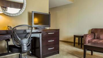 Quarto de hotel com escrivaninha, cadeira, televisão e sofá.