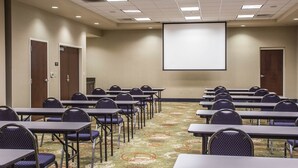 A conference room with rows of tables and chairs, a projector screen, and carpeted flooring. - Comfort Suites Huntersville near Lake Norman (Huntersville)
