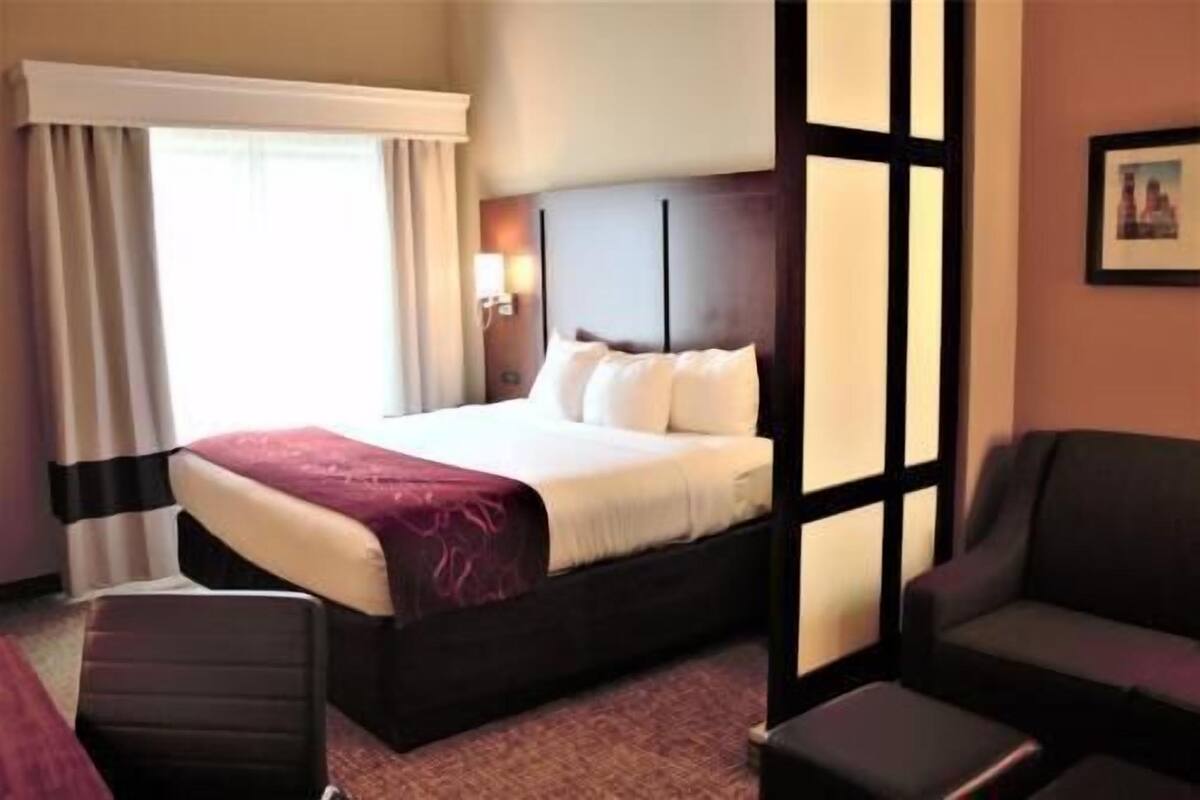 Une chambre d’hôtel avec un lit, une chaise, un bureau et une fenêtre avec des rideaux.