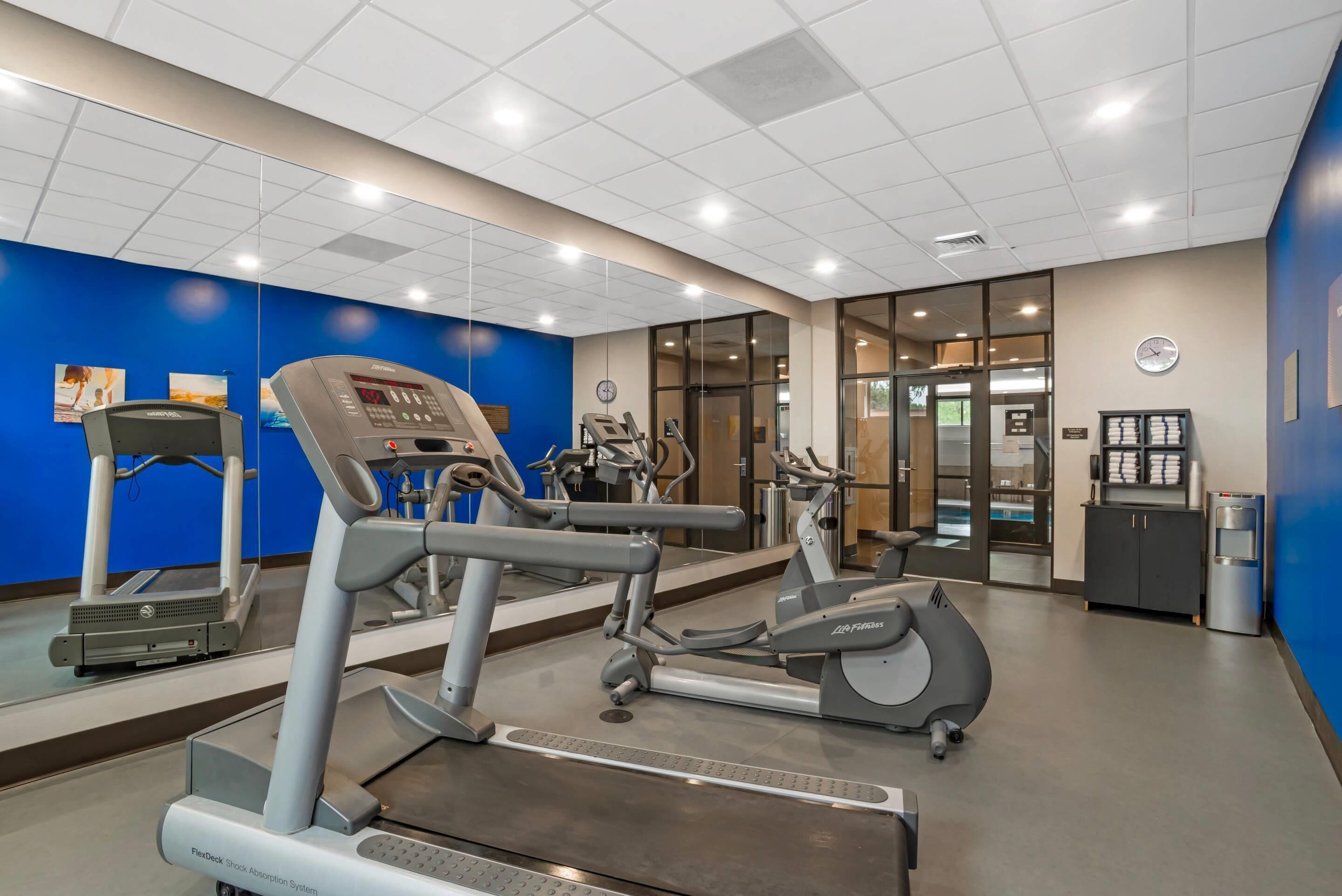 Un centre fitness amb màquines cardiovasculars, un dispensador d'aigua i un rellotge a la paret.
