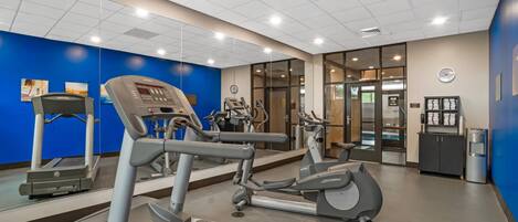 A fitness center with cardio machines, a water dispenser, and a clock on the wall.