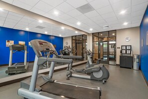Une salle de sport équipée d’appareils de cardio, d’un distributeur d’eau et d’une horloge murale.