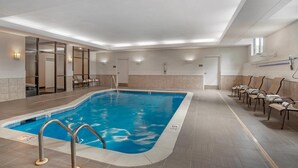 Piscina interna de hotel com água cristalina, prancha de mergulho e espreguiçadeiras.