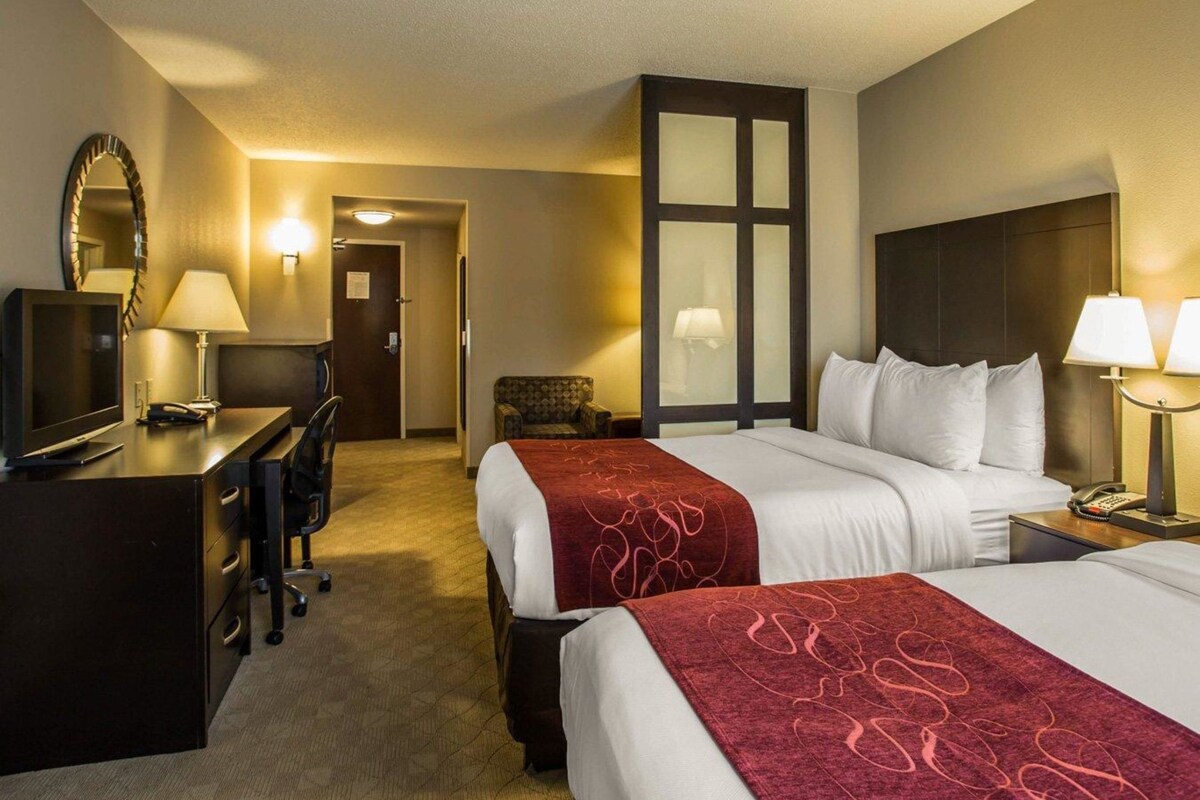Une chambre d’hôtel avec deux lits, un bureau avec une télévision, une chaise et un grand miroir.