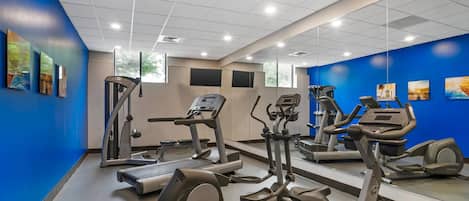 A gym with cardio machines, mirrors, and artwork on the walls.