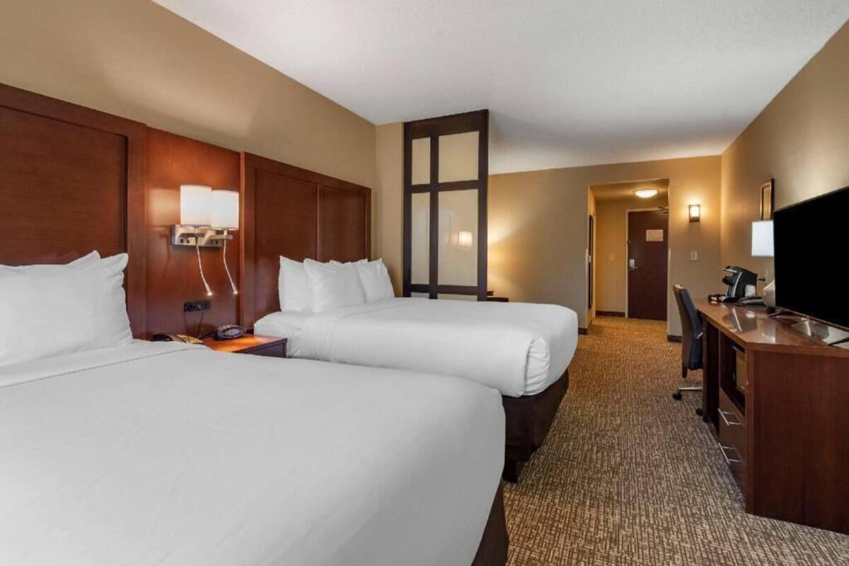 Une chambre d’hôtel avec deux lits, un bureau, une télévision et une porte donnant sur une autre chambre.