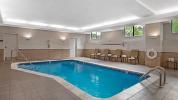 A swimming pool with a 5 ft depth, surrounded by lounge chairs and a lifebuoy, with a view of trees through the windows.