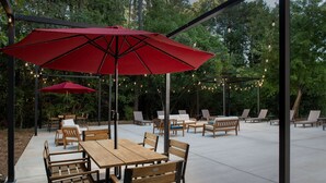 An outdoor patio area with wooden tables and chairs, red umbrellas, and string lights. - Doubletree by Hilton Chattanooga Hamilton Place (Chattanooga)