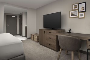 A modern hotel room with a large bed, a wooden desk, a flat-screen TV, and a chair. There are framed pictures on the wall and a door to the left. - Doubletree by Hilton Chattanooga Hamilton Place (Chattanooga)