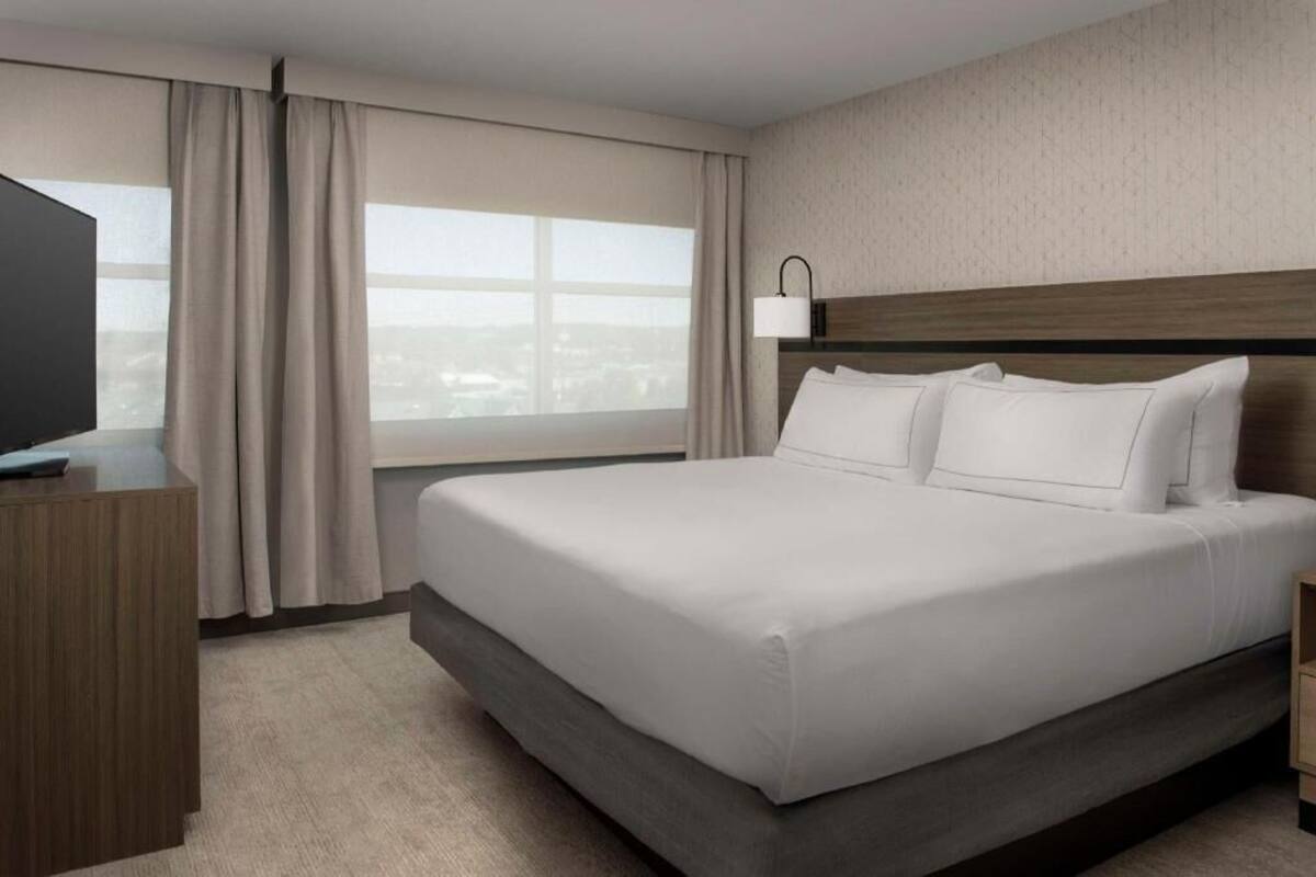 A hotel room with a large bed, a desk, a lamp, and a window with curtains.