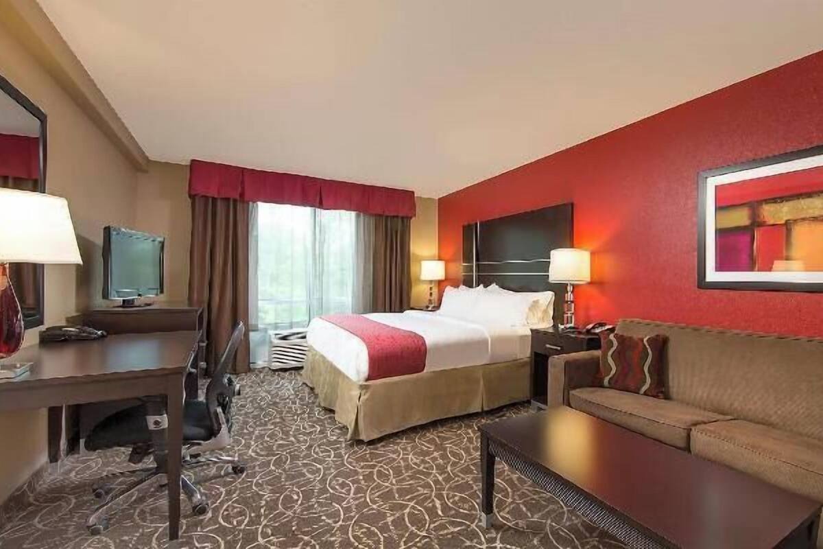 A hotel room with a bed, a sofa, a desk, a chair, a TV, and a large painting on the wall.
