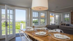 Un coin repas avec une table en bois dressée pour quatre personnes, de grandes fenêtres et une vue sur l’extérieur.