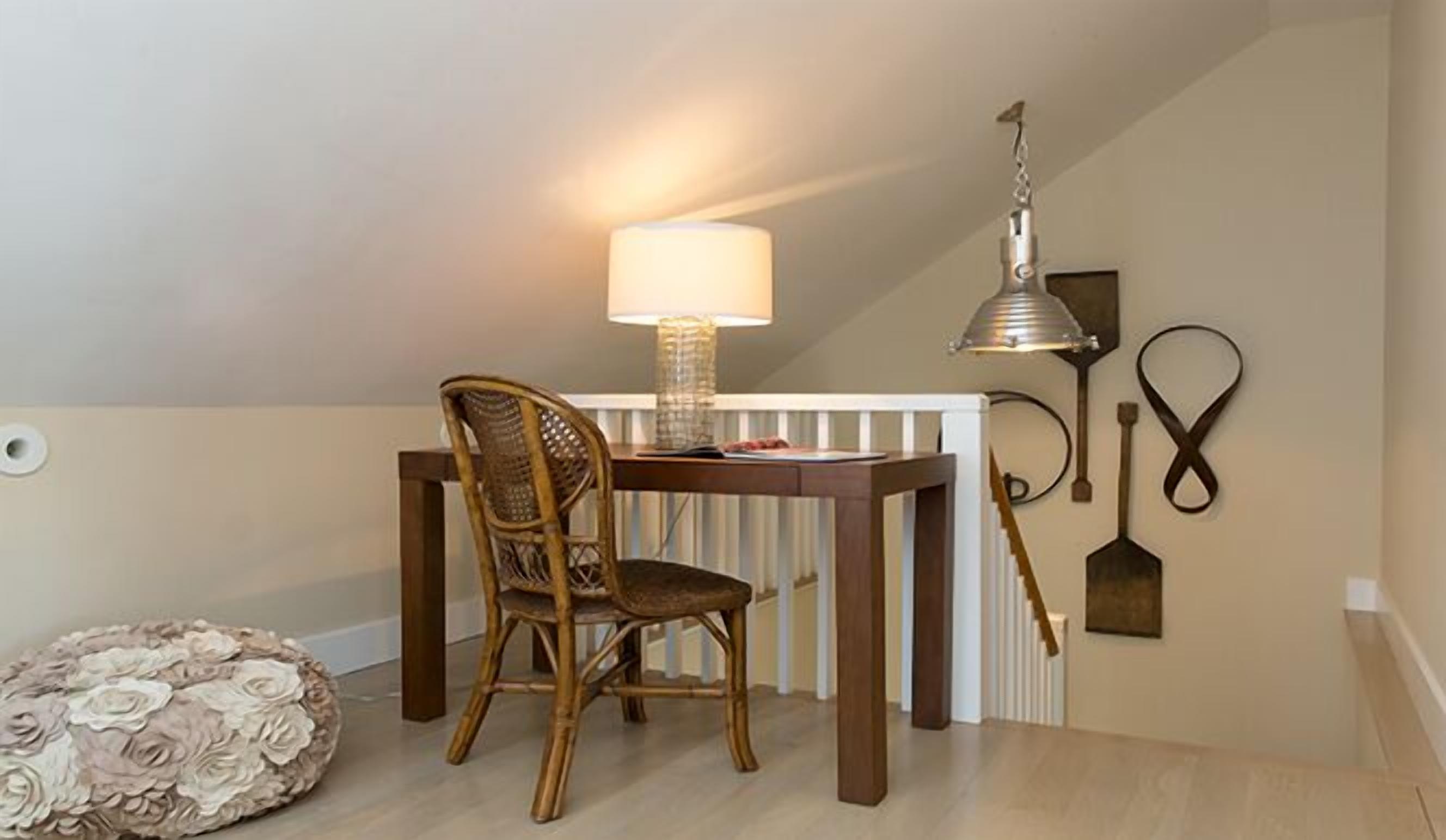 Uma pequena área de refeições com uma mesa de madeira, uma cadeira de vime, um abajur e um objeto decorativo na parede.