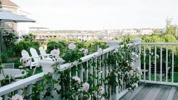 Une terrasse en bois avec des balustrades blanches, des chaises blanches et des roses roses.