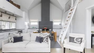 A modern kitchen with white cabinets, a dining area with a wooden table, and a staircase.