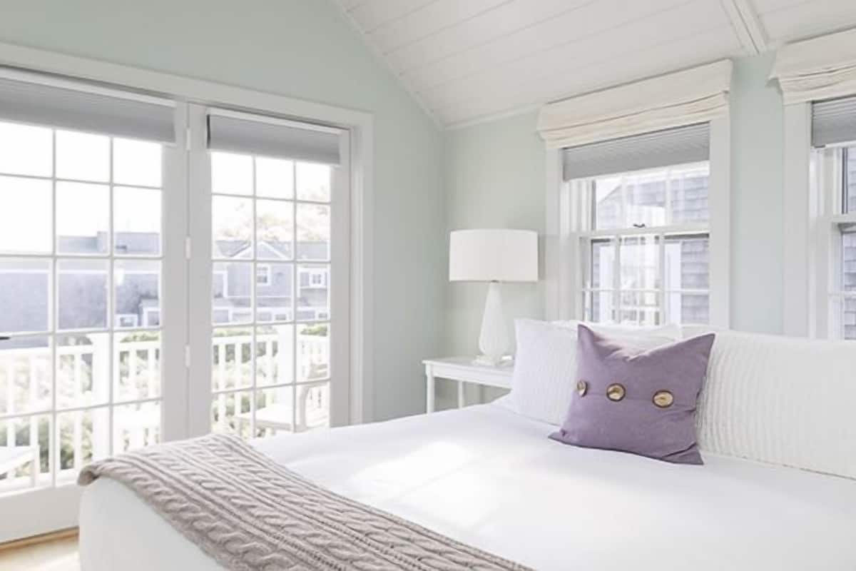 Un dormitorio con una cama grande, una mesita de noche, una lámpara y vistas a través de una ventana.