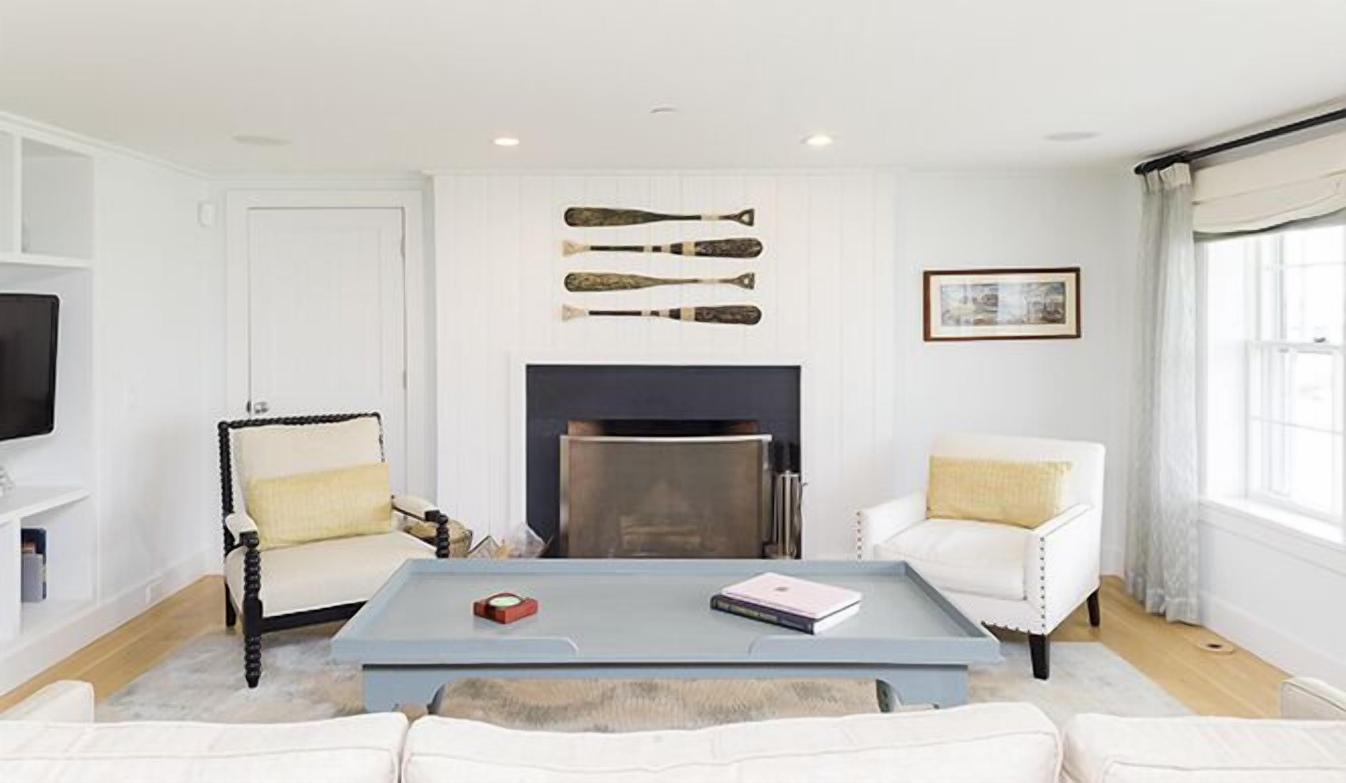 A living room with a fireplace, white furniture, and a coffee table with books and a remote control.