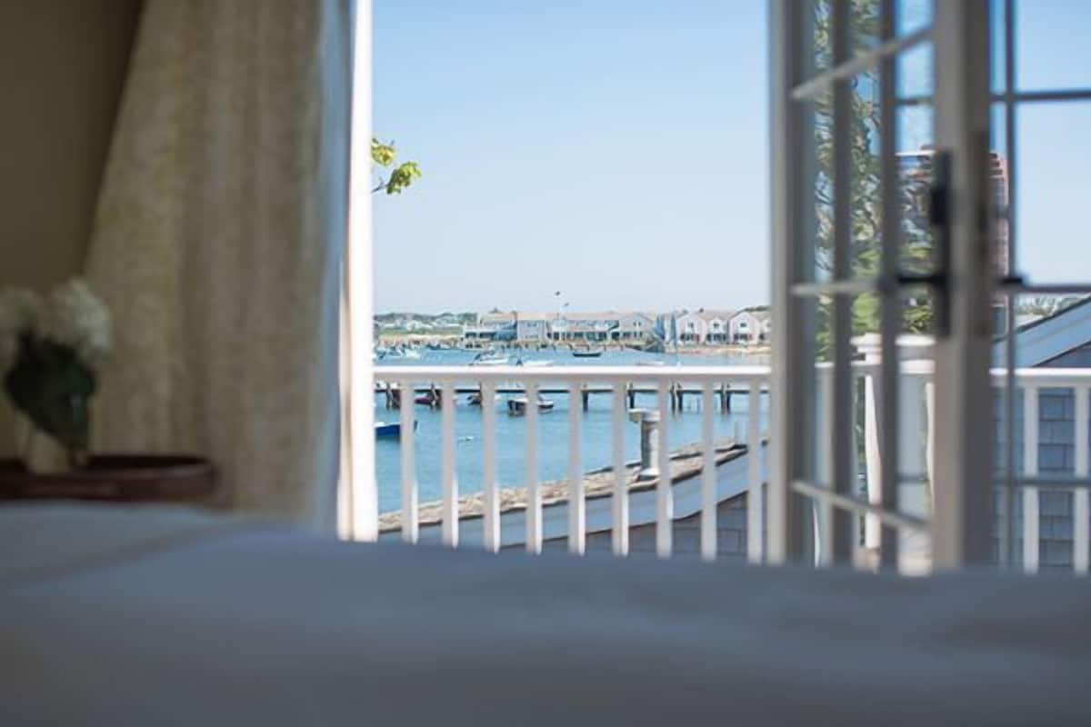 Vista desde una habitación con un amplio ventanal que da a un puerto deportivo con barcos y edificios.
