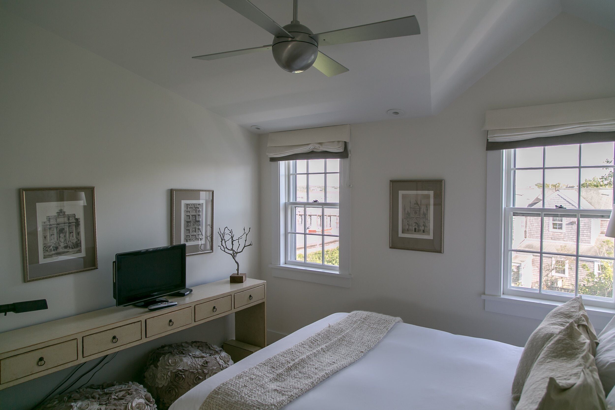 A bedroom with a bed, a desk, a television, and framed pictures on the wall.