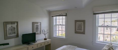 A bedroom with a bed, a desk, a television, and framed pictures on the wall.