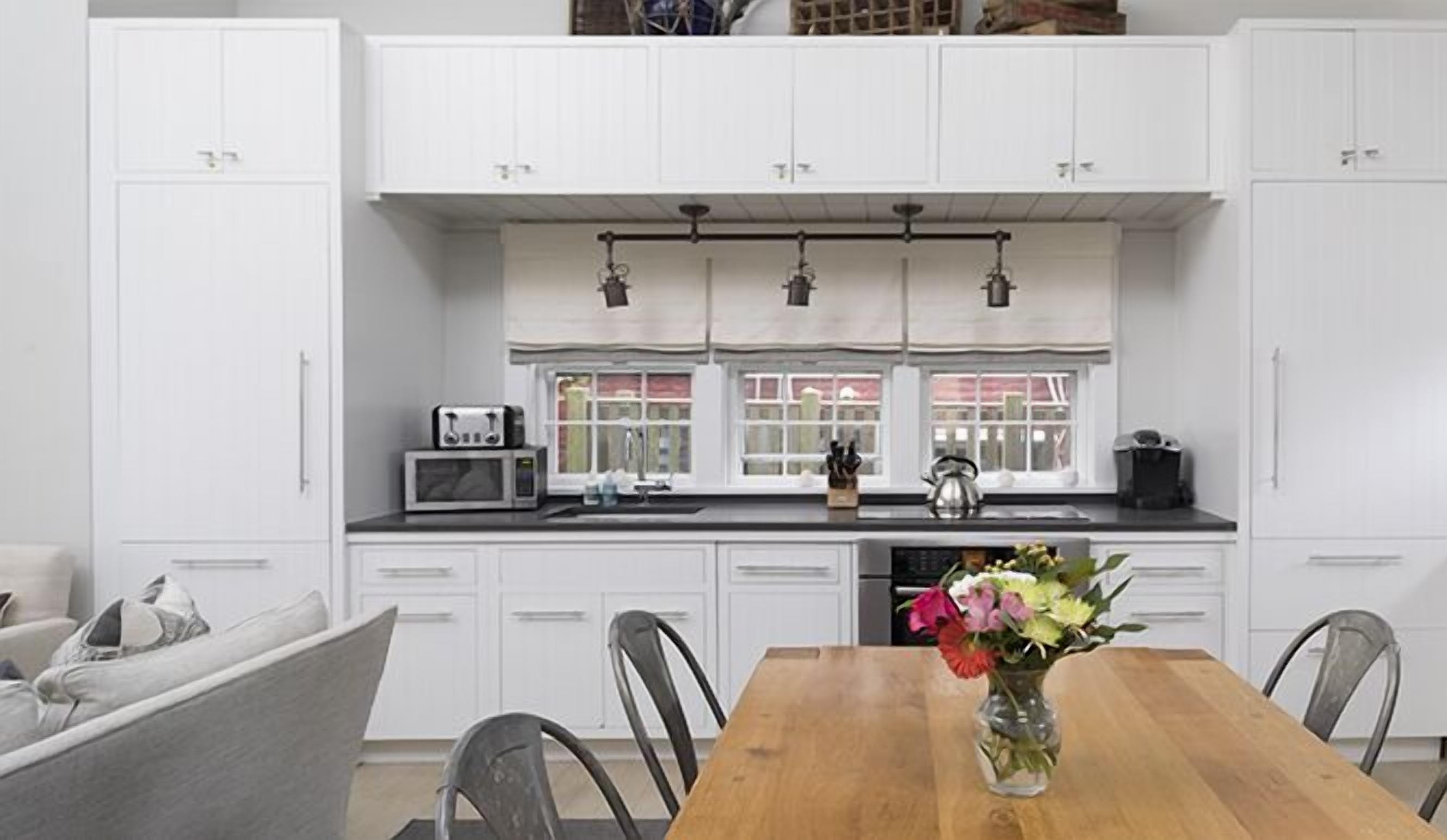 A modern kitchen with white cabinets, a wooden dining table, and a vase of flowers.