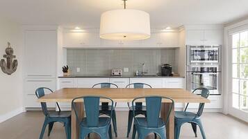 A modern kitchen with white cabinets, a wooden dining table, and teal chairs.