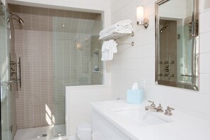 Une salle de bain moderne avec une douche à parois de verre, un lavabo blanc avec un miroir et un porte-serviettes avec des serviettes pliées.
