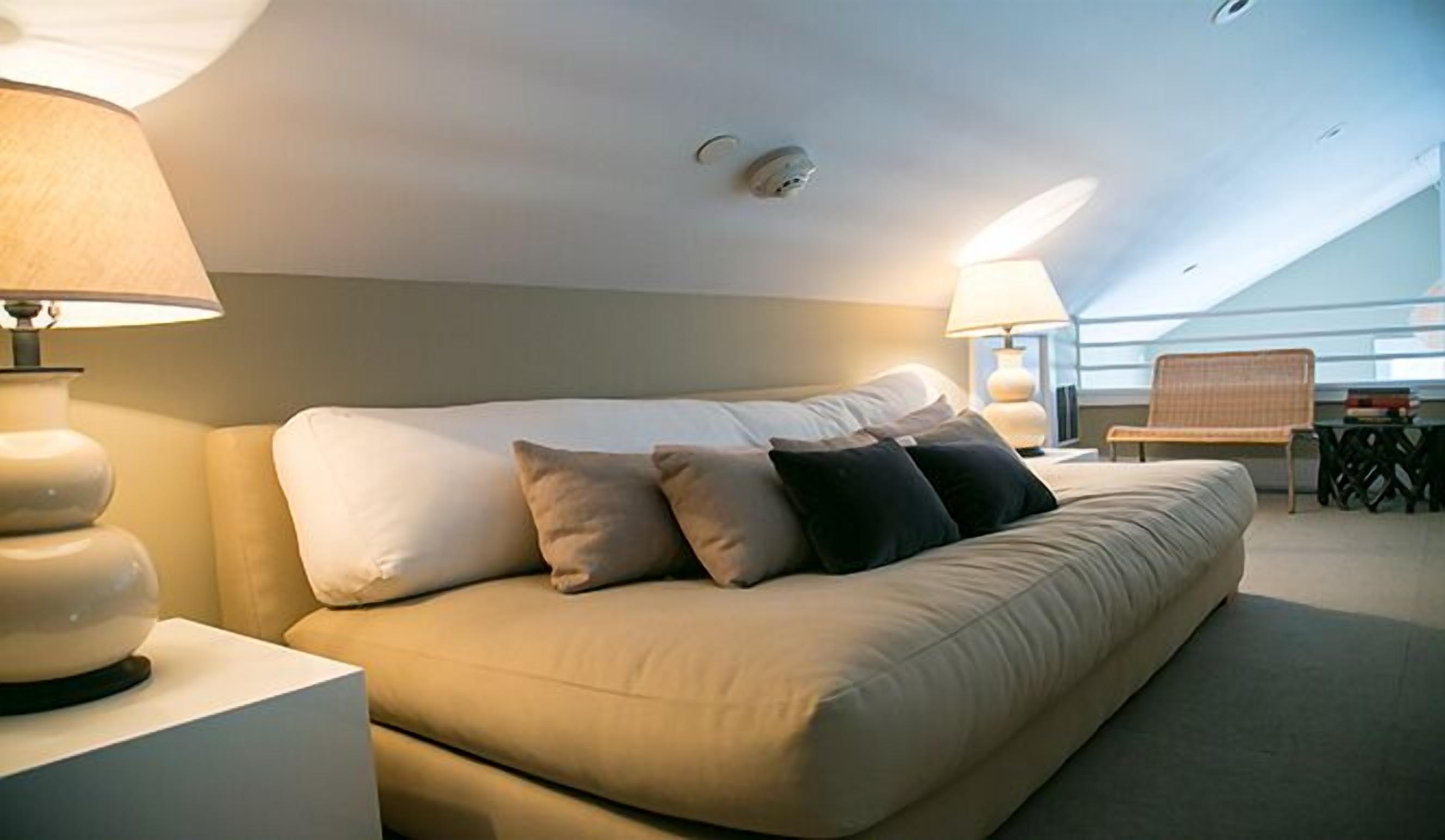 Ett modernt hotellrum med en stor säng, två sängbord med lampor, ett litet bord med en stol och utsikt mot himlen genom taket.