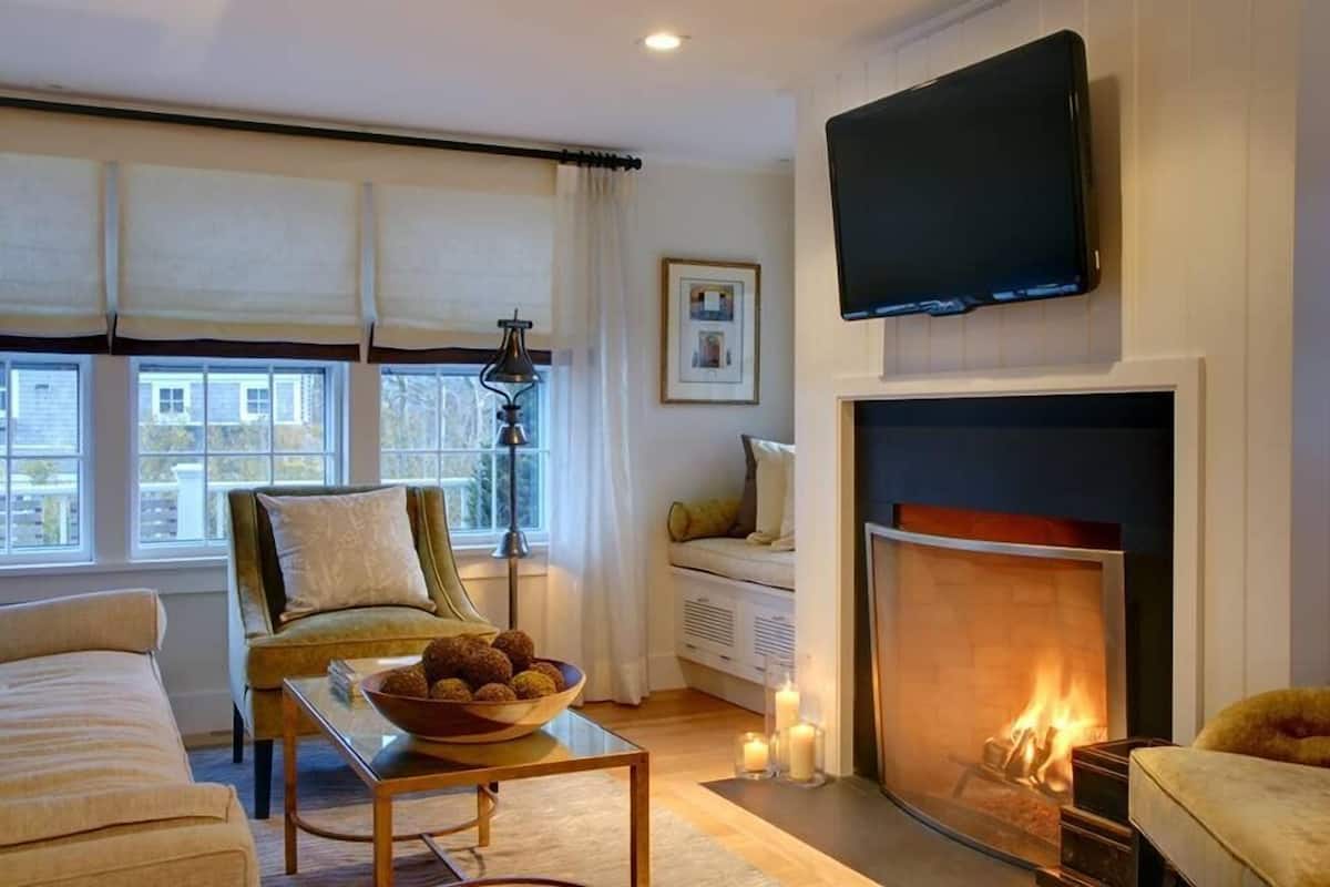 Un salón acogedor con chimenea, un sofá, una mesa de centro con un cuenco de aperitivos y un televisor montado en la pared.