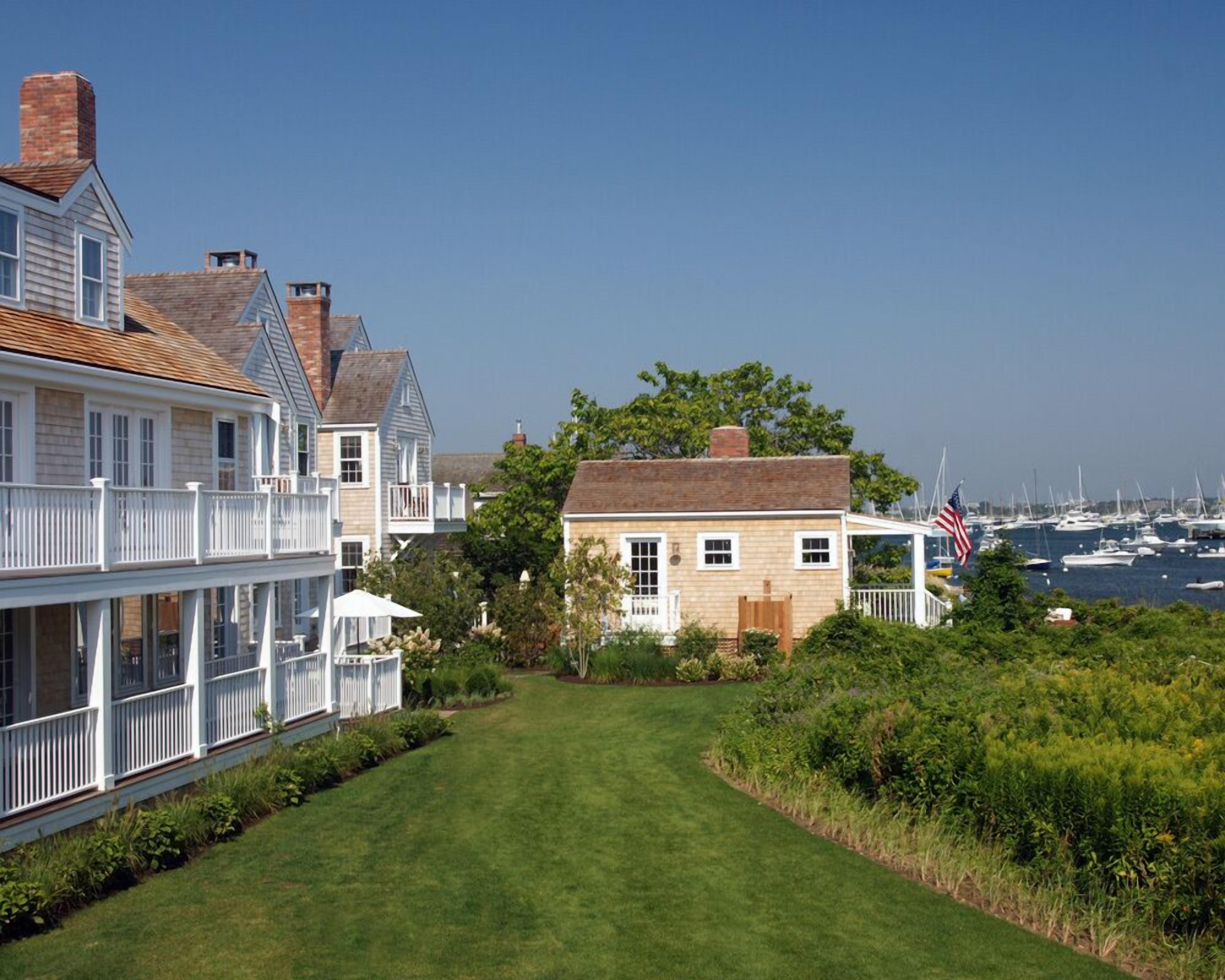 Een woongebied aan de kust met een gazon, een klein huis met veranda en zicht op boten in de verte.