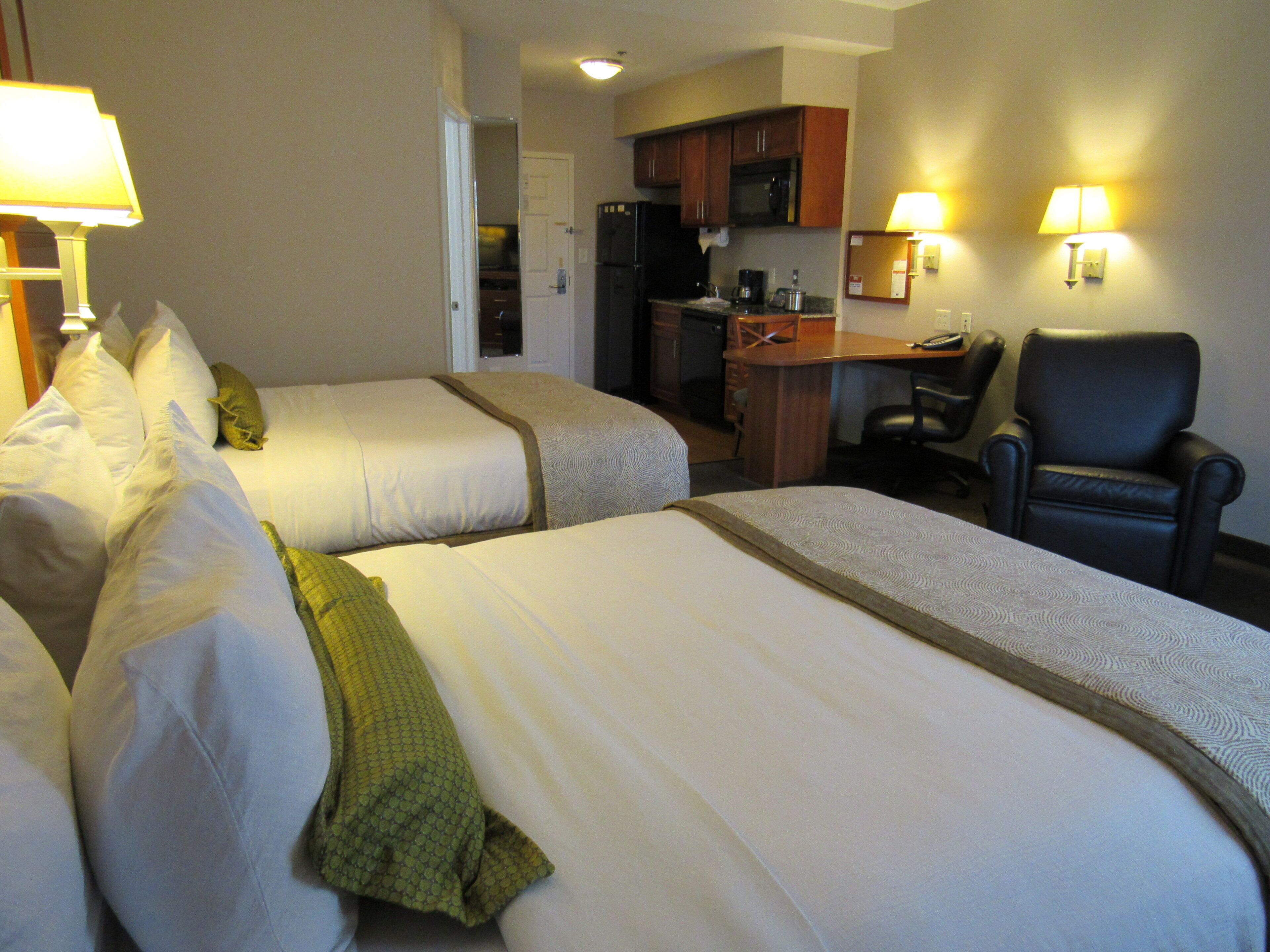 Een hotelkamer met twee bedden, een bureau, een stoel en een kitchenette.