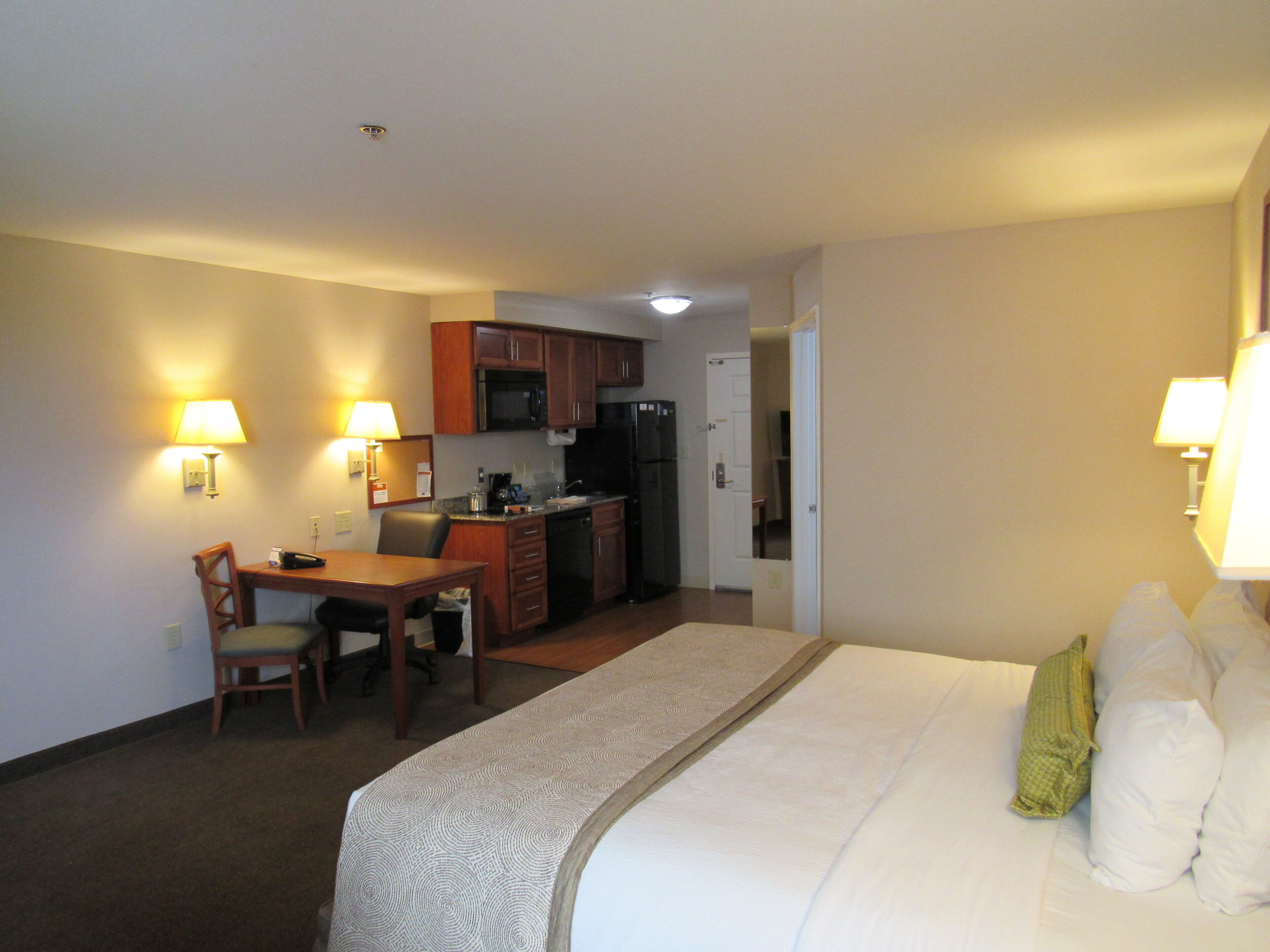 A hotel room with a bed, a desk, a chair, a microwave, a refrigerator, and a small kitchenette.