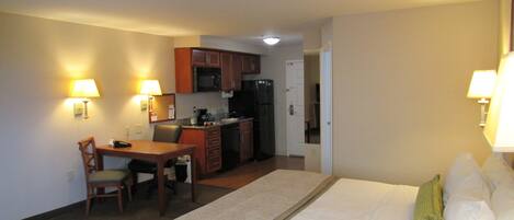 A hotel room with a bed, a desk, a chair, a microwave, a refrigerator, and a small kitchenette.