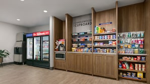A kitchen area with a refrigerator, microwave, and shelves stocked with various food items. - Candlewood Suites Murfreesboro by IHG (Murfreesboro)