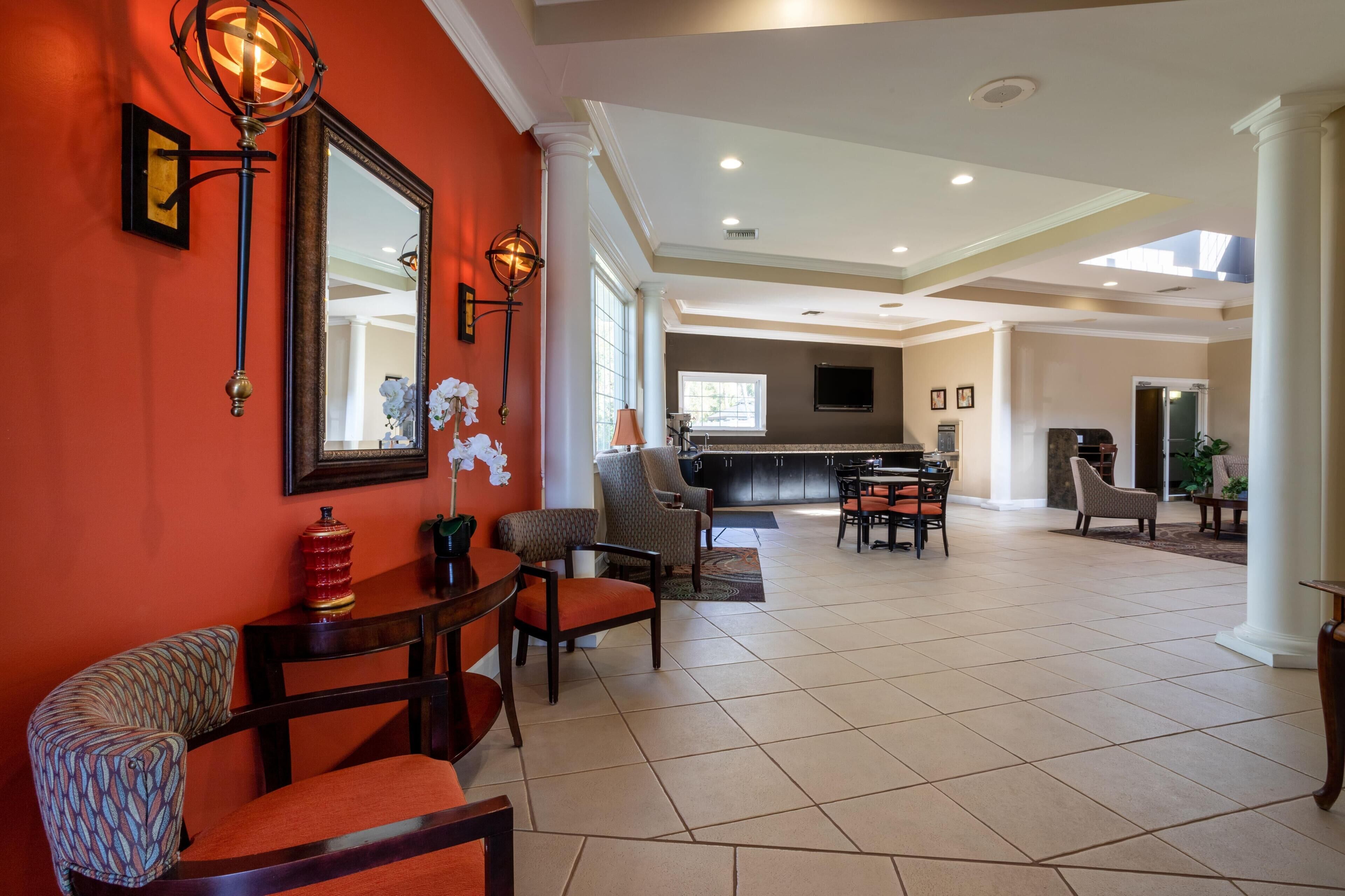 A spacious living area with a kitchen in the background, a large mirror, and a modern chandelier.