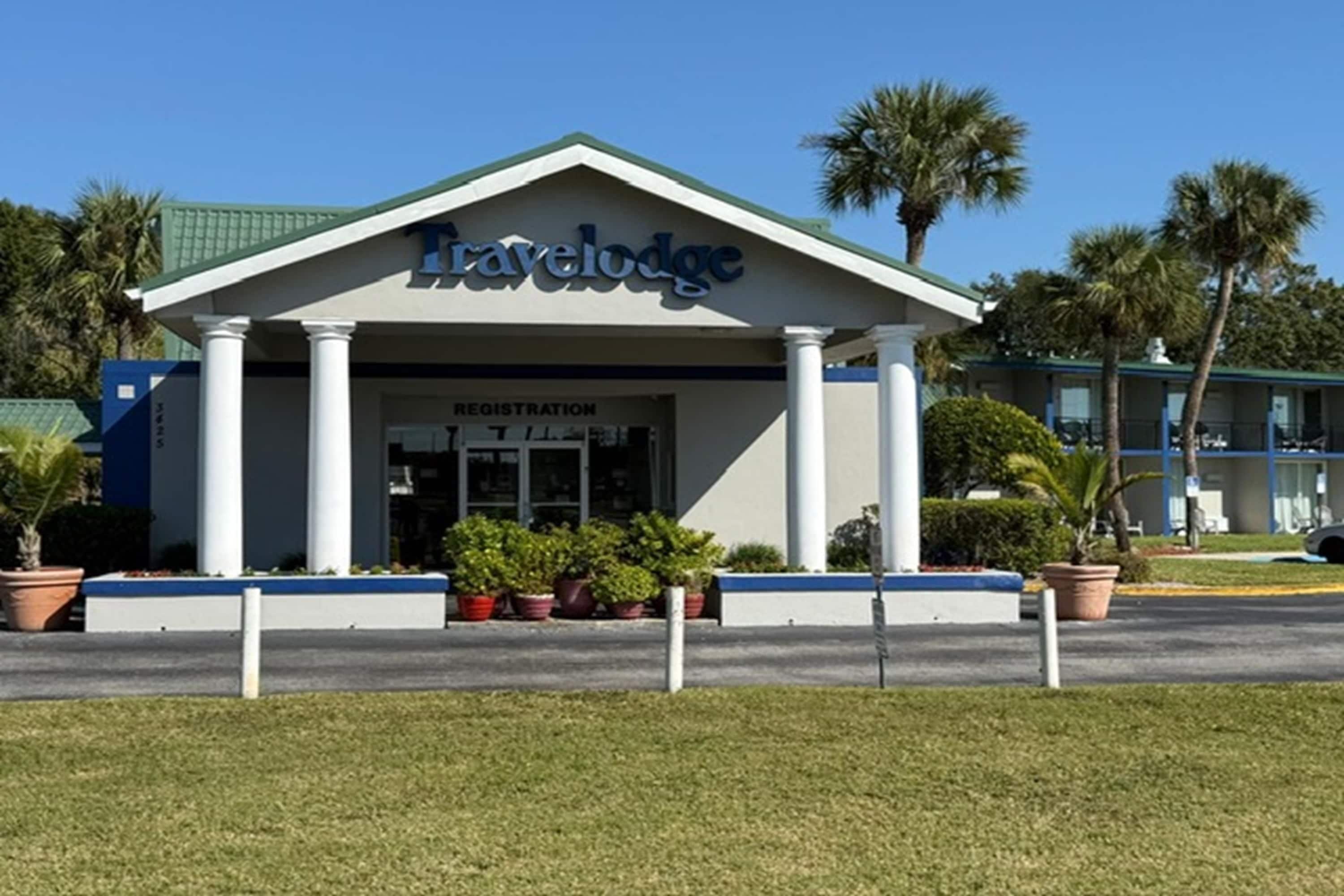 Een Travelodge gebouw met een receptiebord, zuilen en bloempotten.