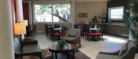A spacious lobby with multiple seating areas, including sofas and chairs, a coffee station, and a reception desk.
