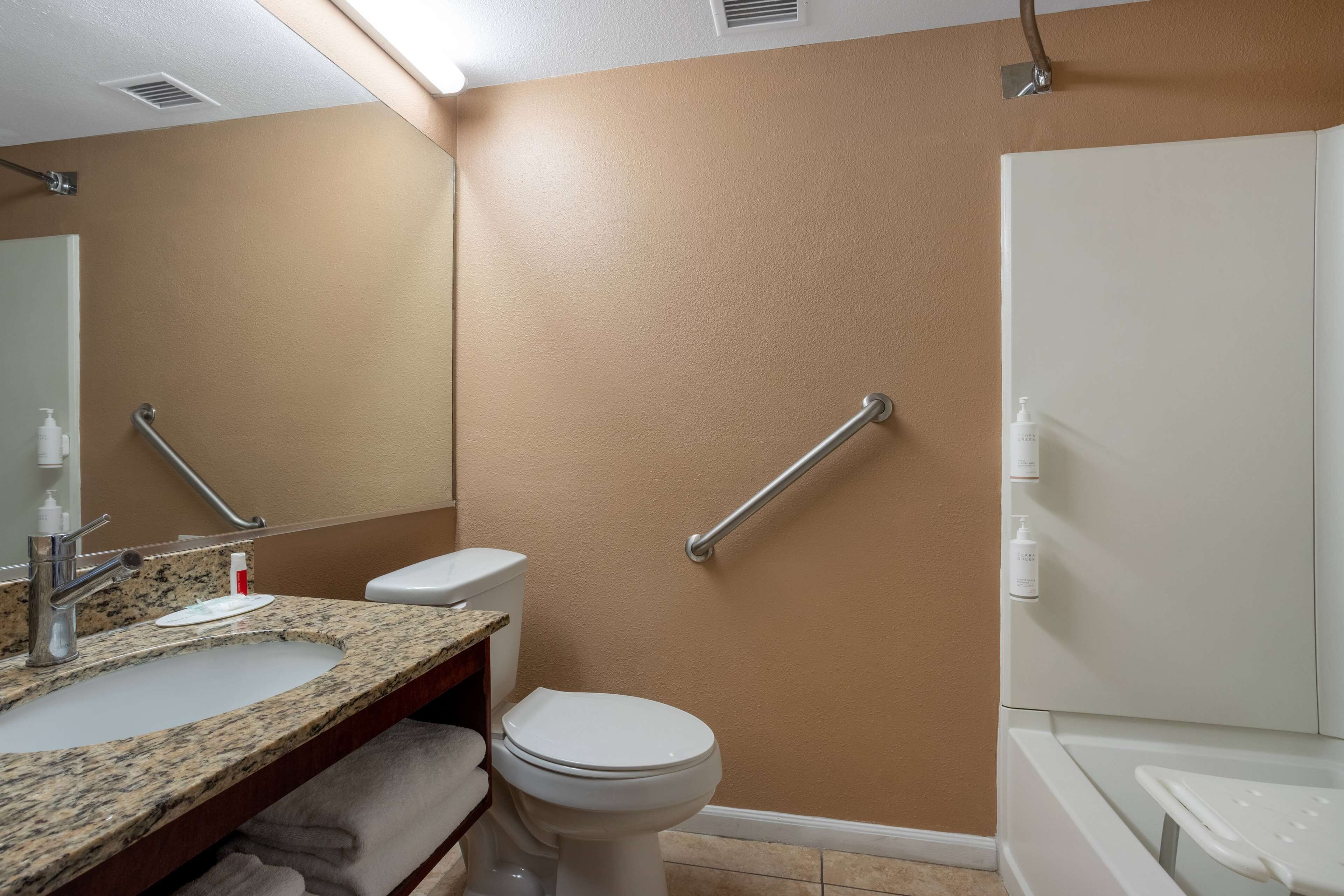 A bathroom with a beige wall, a white toilet, a sink with a granite countertop, and a white bathtub.