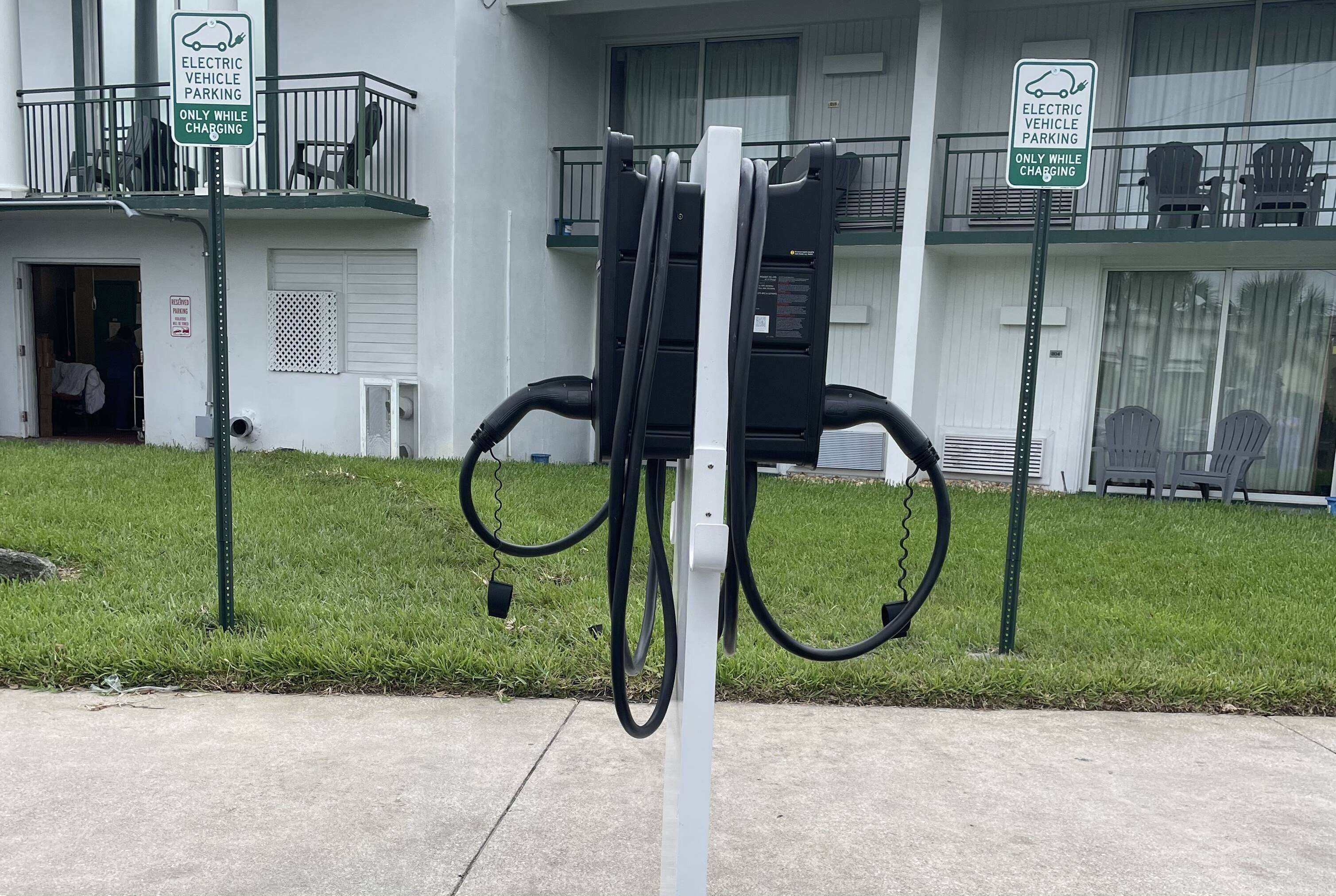 Una stazione di ricarica per veicoli elettrici di fronte a un edificio con un balcone e posti a sedere all'aperto.