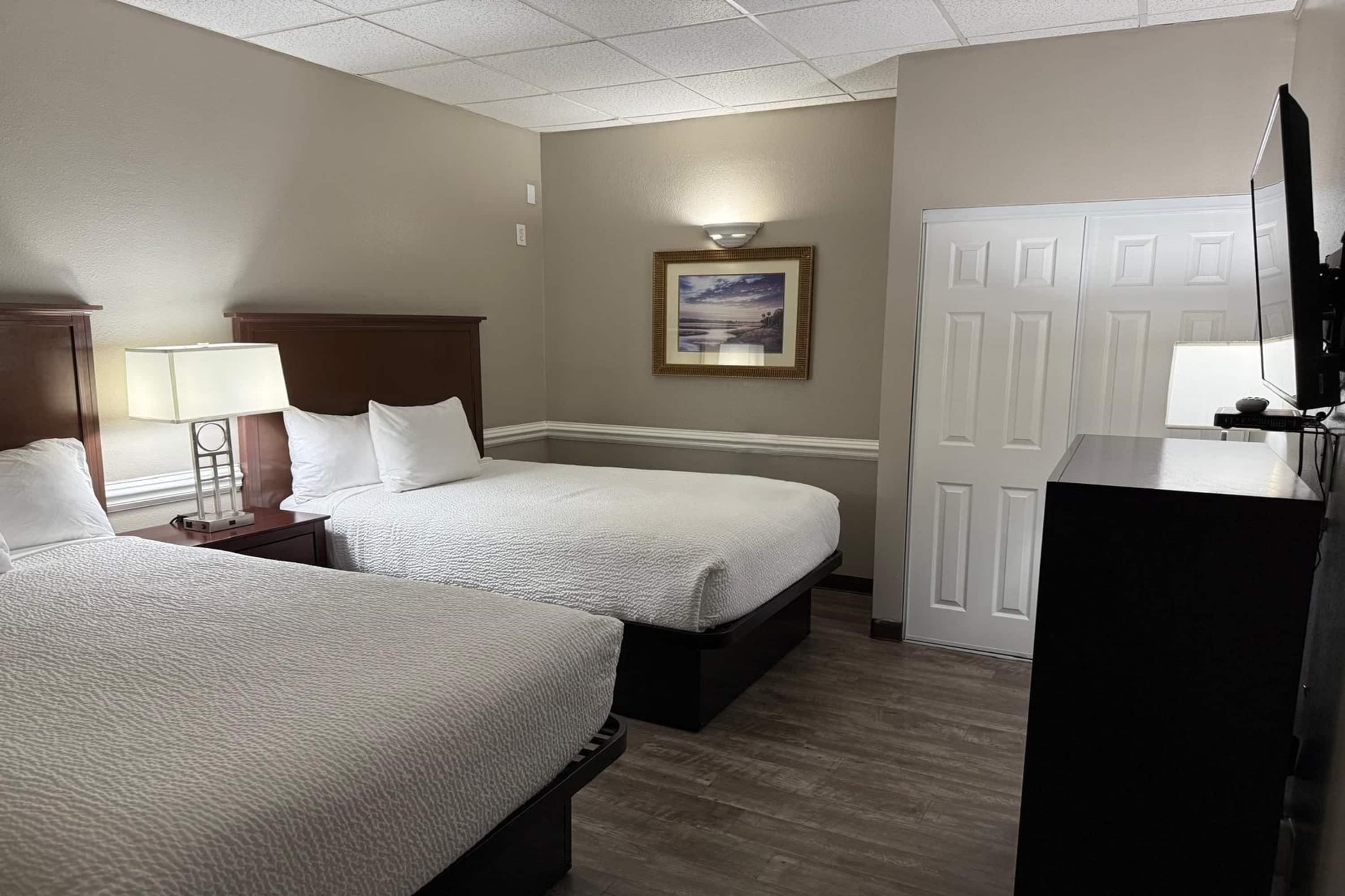 A hotel room with two beds, a desk with a lamp, a TV, and a framed picture on the wall.
