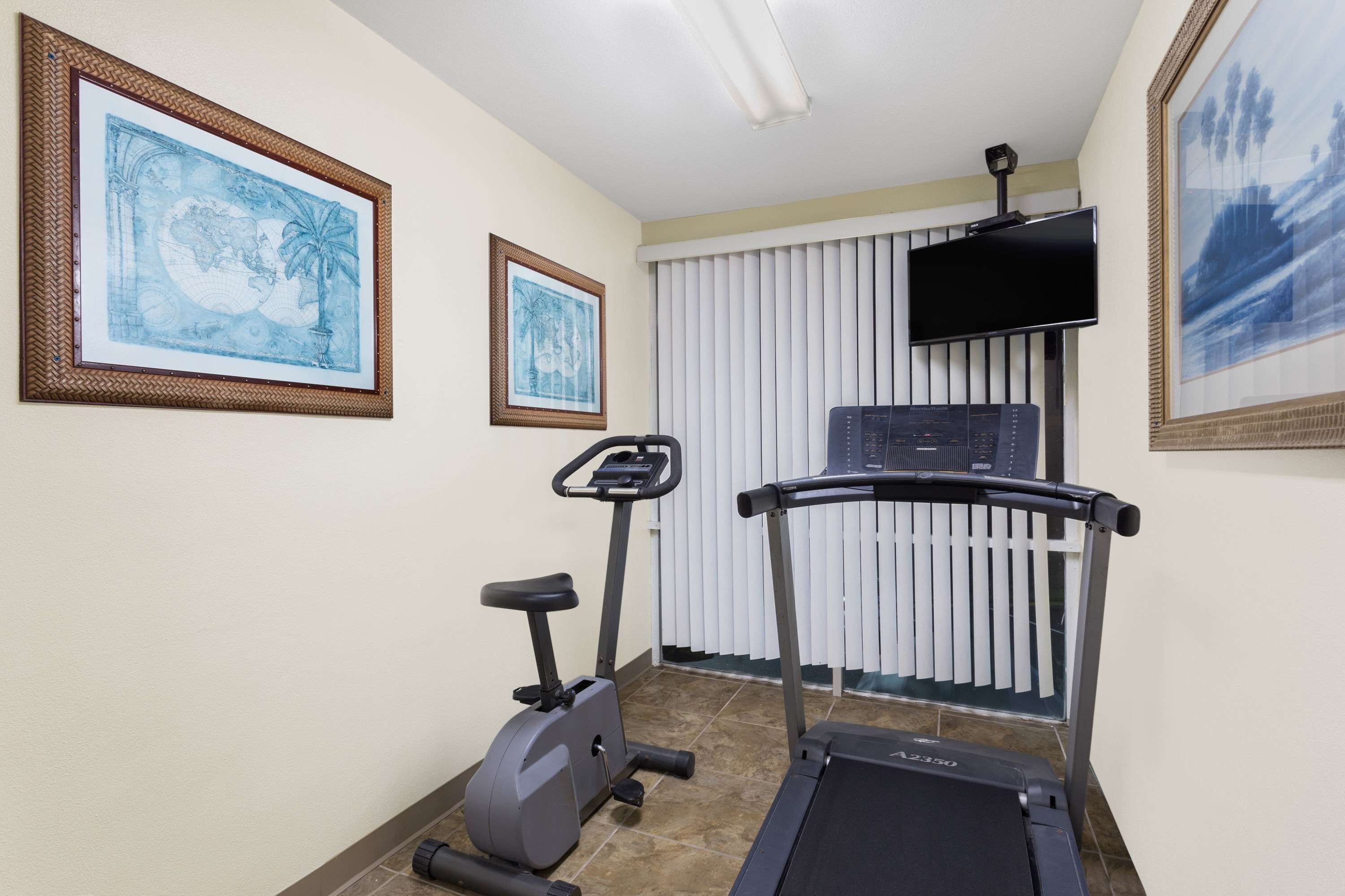 A fitness room with a treadmill, an elliptical, and framed artwork on the walls.