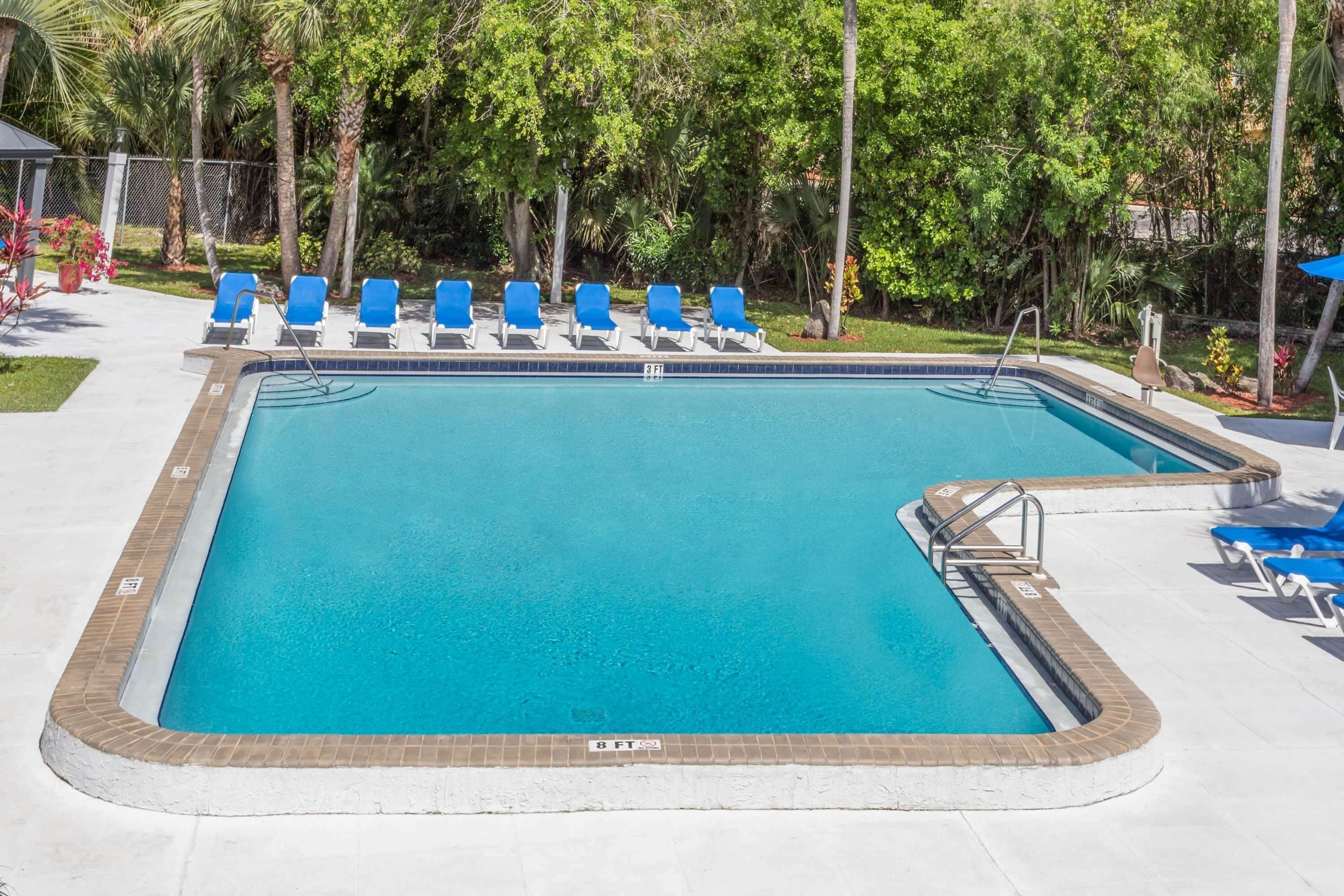 A rectangular swimming pool with a tiled edge, surrounded by blue lounge chairs and a brick border.