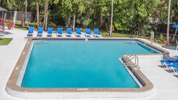 A rectangular swimming pool with a tiled edge, surrounded by blue lounge chairs and a brick border.