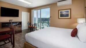 A hotel room with a bed, a desk with a TV, a balcony with chairs, and a painting on the wall. - Travelodge by Wyndham Lakeland (Lakeland)