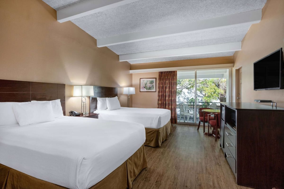 Habitación de hotel con dos camas, un escritorio, televisión y balcón con vistas.