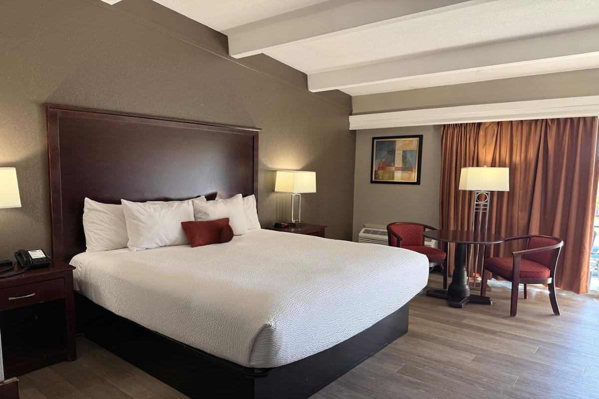 Una habitación de hotel con una cama grande, mesitas de noche, un escritorio con una silla, una lámpara y un cuadro en la pared.